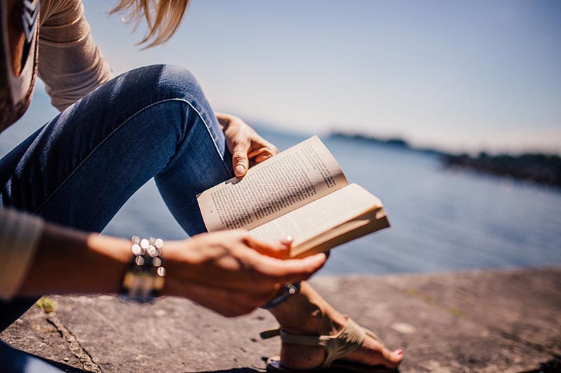 Jeune femme lit un livre au bord de la mer