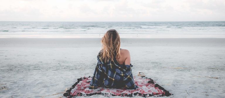 Femme de dos assise sur la plage face à la mer