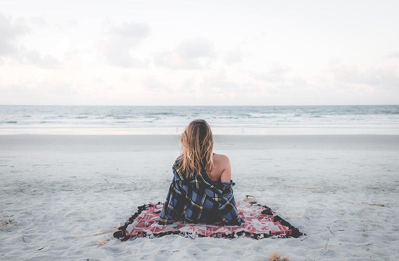 femme assise sur la plage face à l'océan