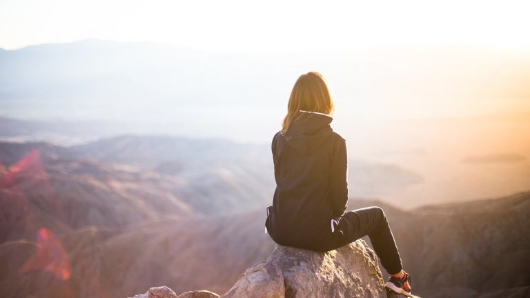 Femme assise sur un rocher face à une vallée